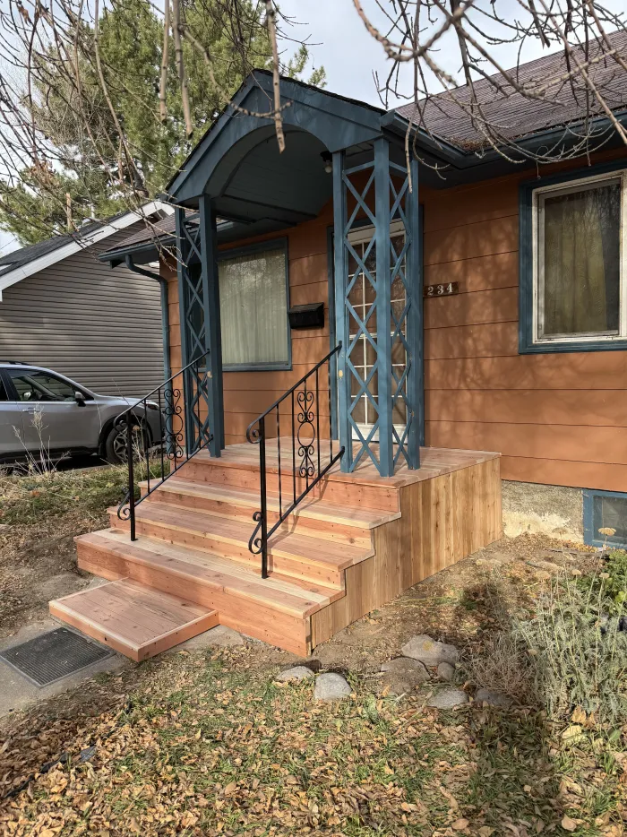 New wooden front steps and landing with a black iron handrail at an orange house.