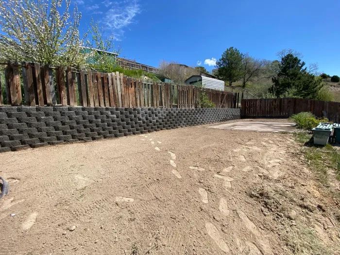 The same yard with a long block retaining wall and freshly graded soil.