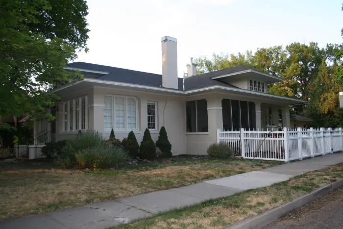 A craftsman bungalow with a dry, patchy front lawn behind a white picket fence.