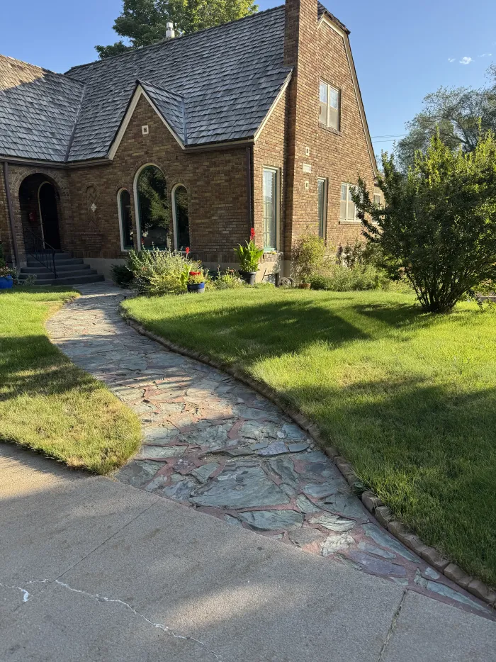 An old, uneven flagstone walk across a lawn to a brick Tudor house.