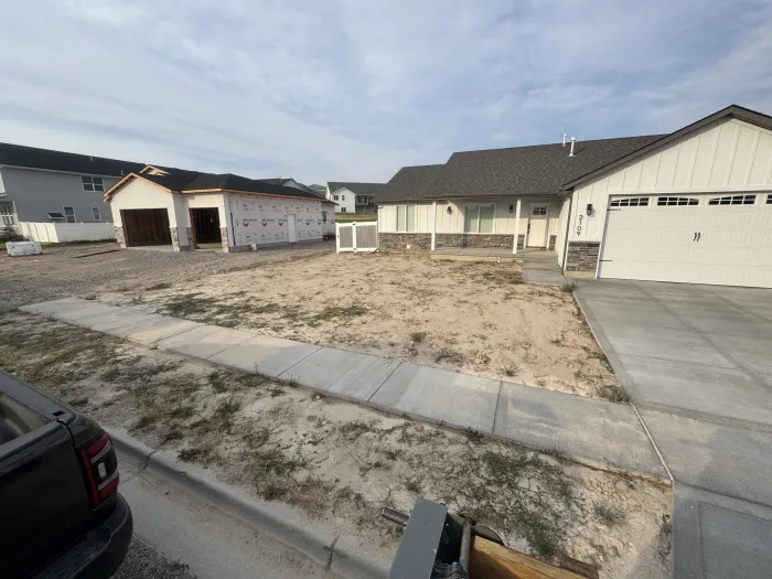 Bare, weedy dirt in front of a newly built house.
