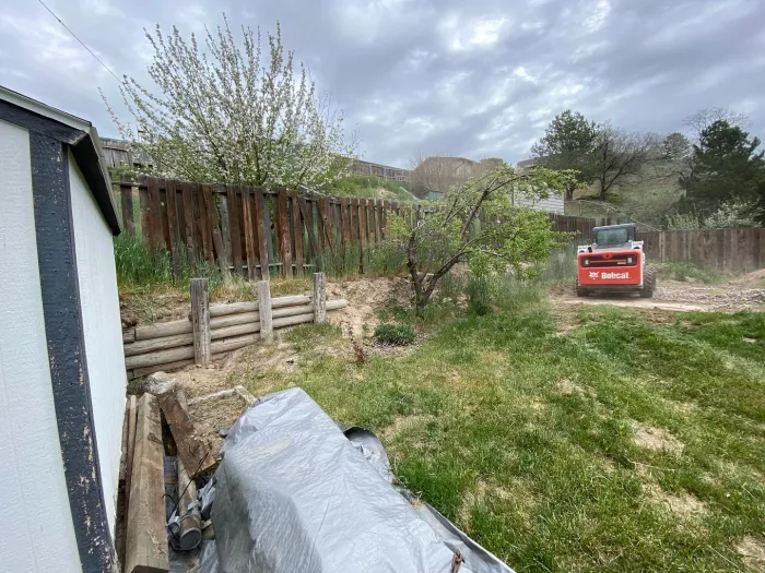 A backyard slope with old railroad tie terraces, weeds and a skid steer at work.