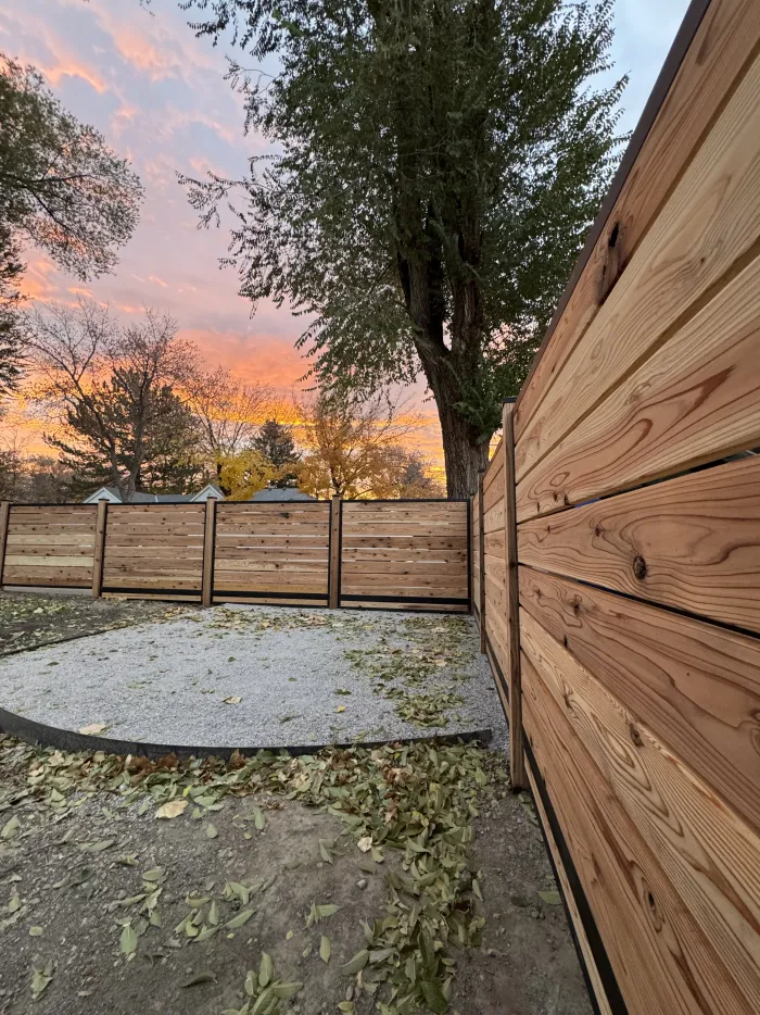 Tall horizontal cedar fence along a side yard with a pink and orange sunset sky.