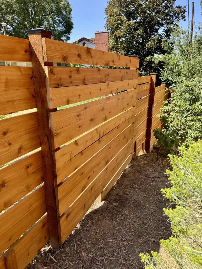 Tall horizontal cedar fence with a cedar post, beside shrubs.