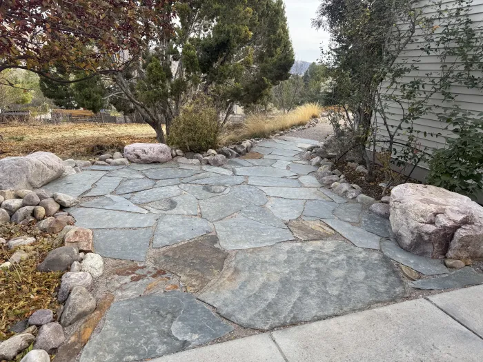 Blue-gray flagstone patio bordered with river rock and boulders beside a house.