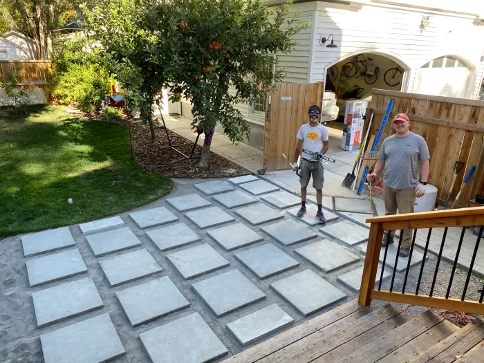 Two men standing on a patio of large square pavers they are laying beside a deck.