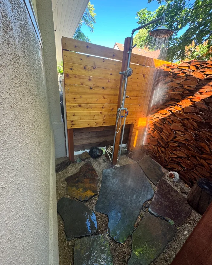 Outdoor shower with a cedar privacy screen and a flagstone floor beside a house.