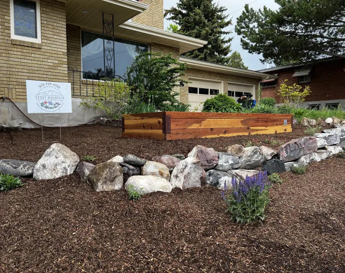 Raised redwood bed above a bank of boulders, mulch and purple flowering plants, with a Scout Mountain yard sign.