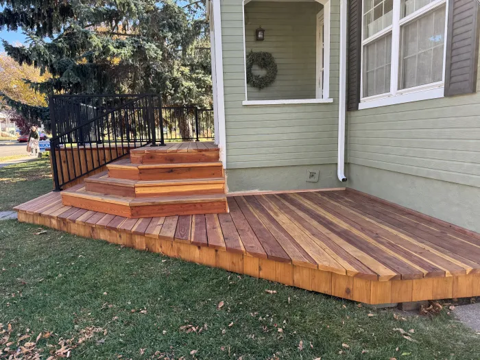 New redwood deck with wide steps down to a lawn, beside a sage green house.