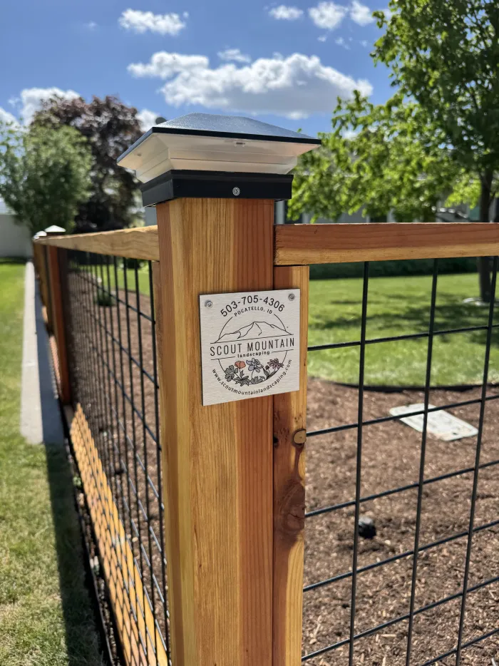 Redwood fence post with a small Scout Mountain Landscaping plaque and a wire panel.
