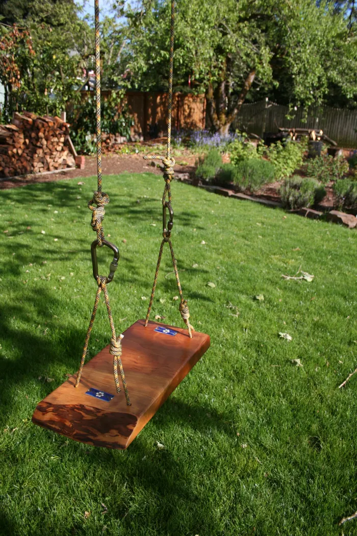 Redwood rope swing with a small tile inlay, hanging over a green lawn.