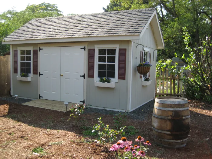 Garden shed with shuttered windows and flower boxes, a wine barrel and pink coneflowers in front.