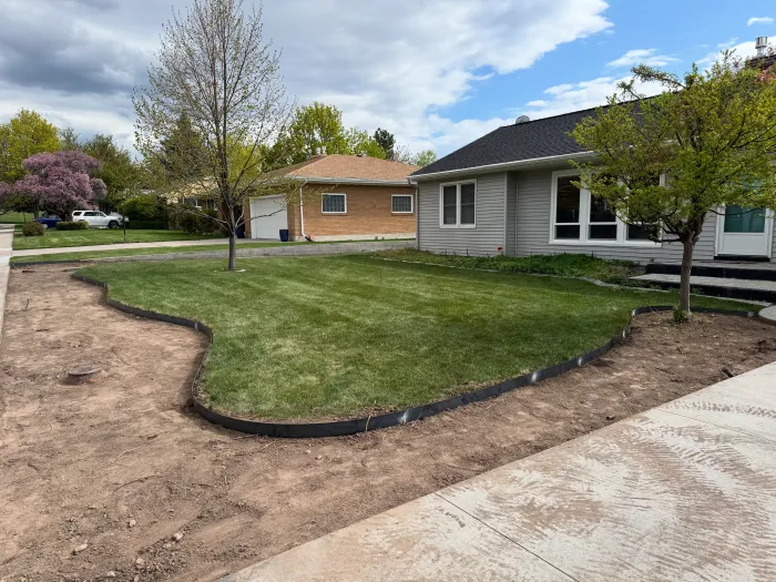 Curving black steel edging between a new lawn and a freshly dug bed in front of a house.