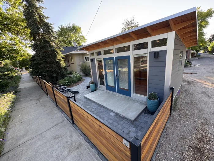 Modern backyard studio with blue French doors, a paver landing and a horizontal cedar fence along the sidewalk.